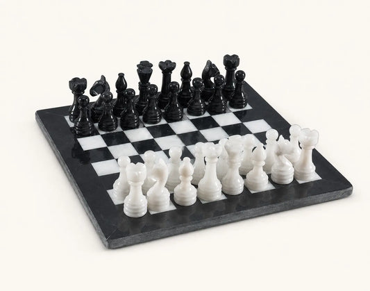 A black and white marble chess set on a light cream background. The set includes a rectangular checkered board with black and white squares, paired with black and white chess pieces shaped like pawns, rooks, knights, bishops, queens, and kings.