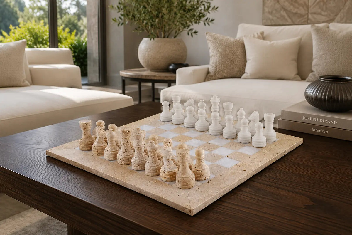A stone chess set with cream-colored wooden pawns and white stone pieces arranged on a checkered board on a dark wood coffee table in a modern living room setting.