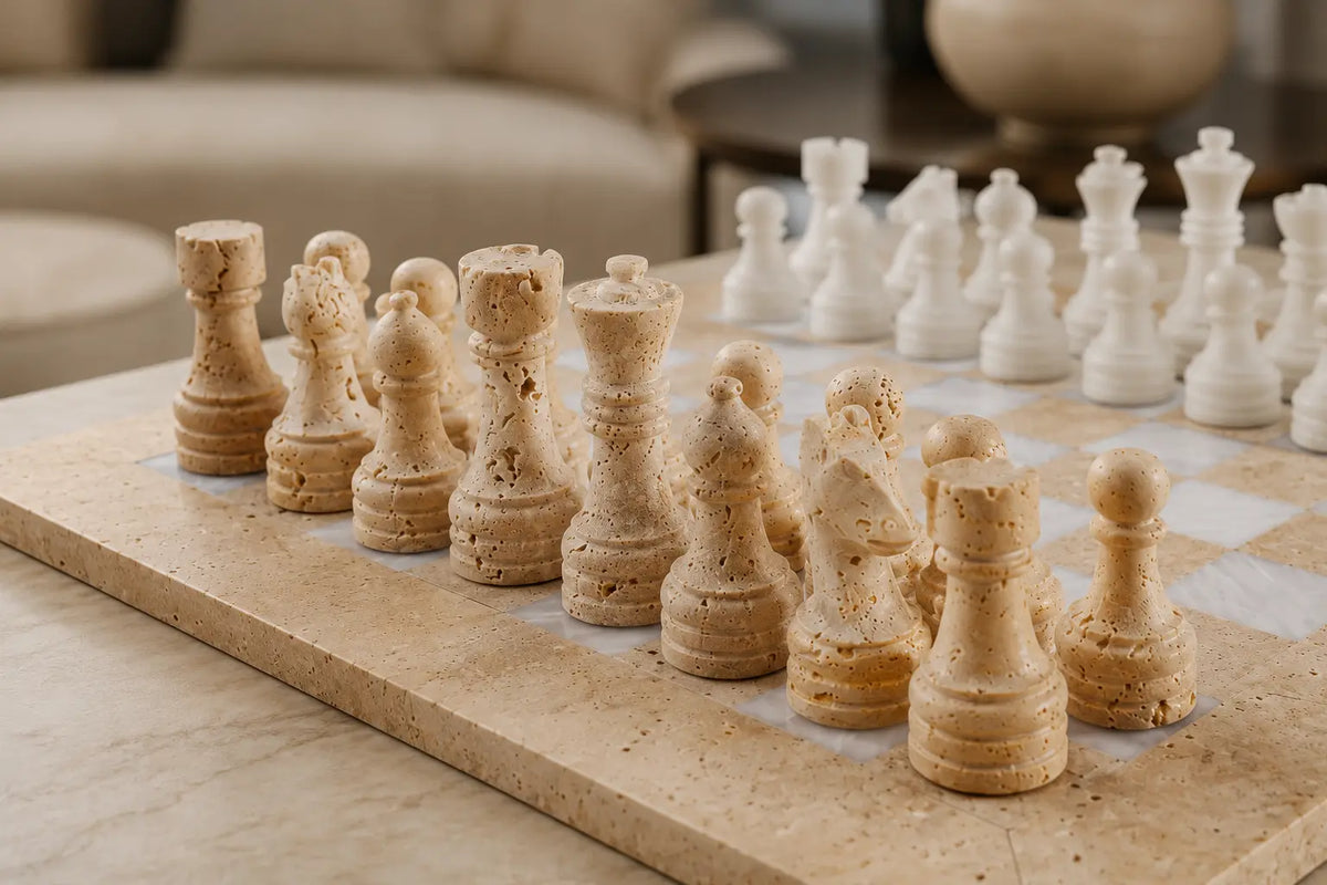 A set of stone chess pieces on a matching stone chessboard, with the beige pieces in the foreground and white pieces in the background, set in a modern living room environment.