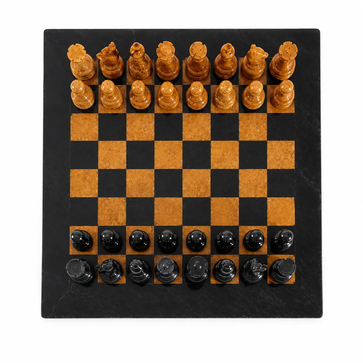 A square chess set on a black stone board with alternating black and warm tan squares, featuring carved light wood chess pieces on the top row and glossy black chess pieces on the bottom, photographed from above on a white background.