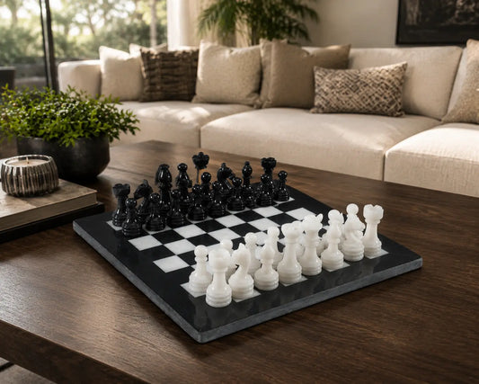 A black and white checkers game set on a dark gray slate board, styled on a dark wood coffee table in a modern living room with a beige sectional sofa in the background.