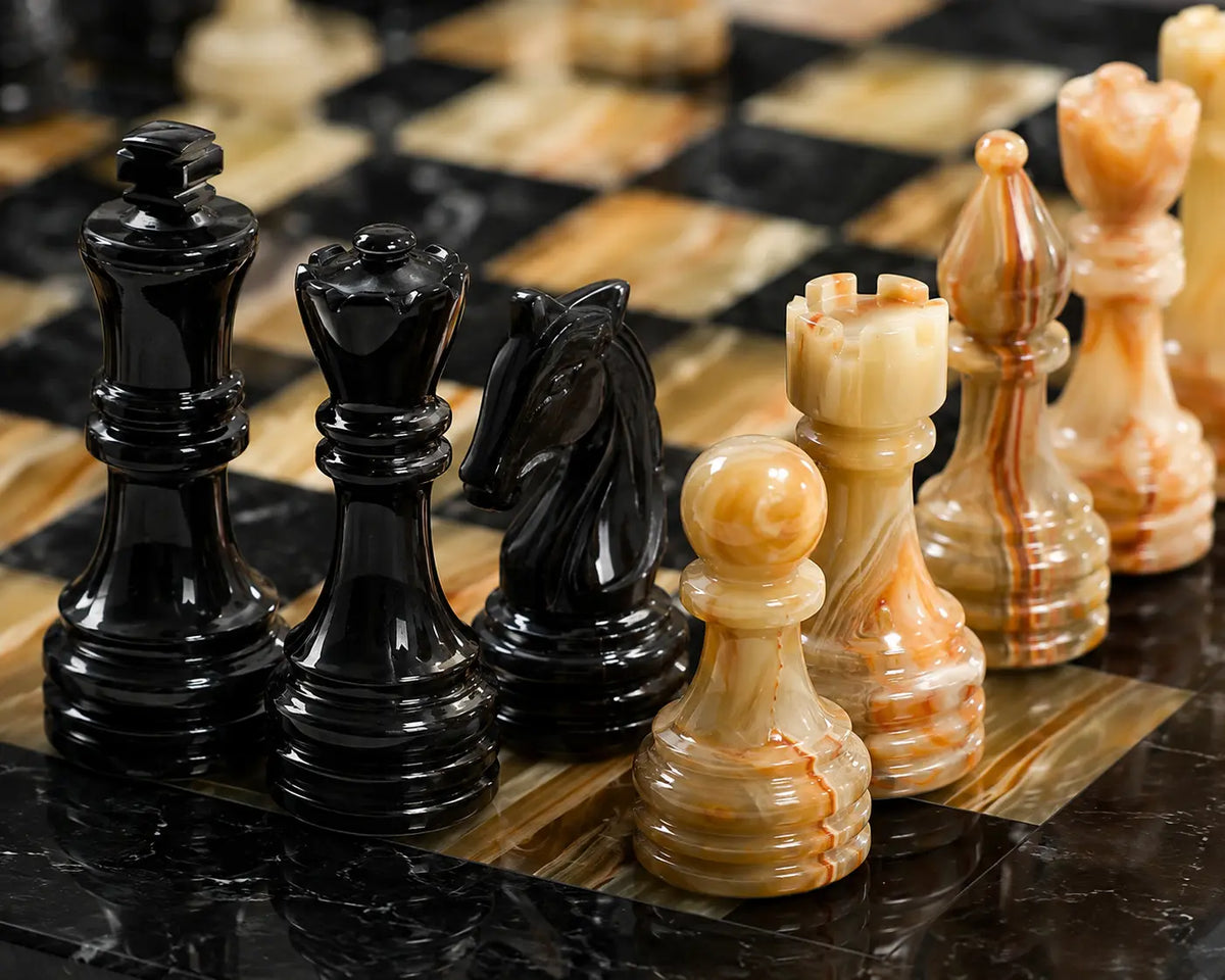 A close-up of a polished stone chess set on a matching marble chessboard, featuring glossy black pieces and cream and tan marbled pieces.